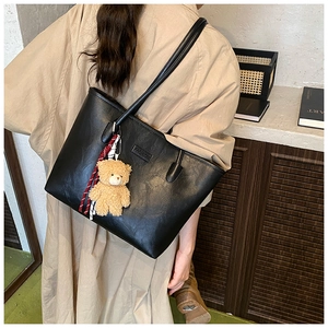 Detail of black tote bag featuring pebbled faux leather texture and plush bear charm