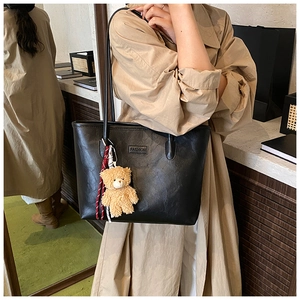 Detail of black leather tote bag featuring a plush bear charm and embossed fashion text