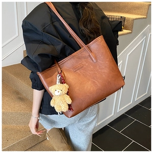 Detailed view of caramel brown tote bag with FASHION logo and plush bear charm on model