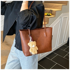 Detail of a brown PU leather tote bag featuring fashion embossing and a cute bear charm