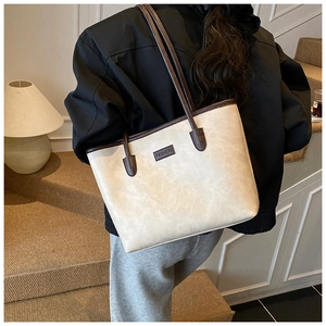 Detail of a large cream tote bag with brown straps and FASHION label worn by a model