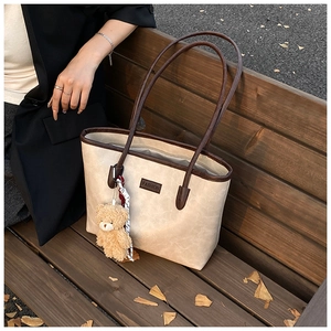 Detail of a cream tote bag featuring brown leather trim and a cute plush bear pendant
