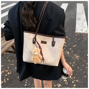 Detail of minimalist beige leather tote with brown straps and cute bear charm in street setting