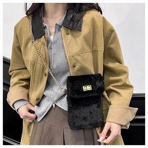 Detail of a black plush crossbody bag with a gold chain strap worn by a model in a trendy outfit