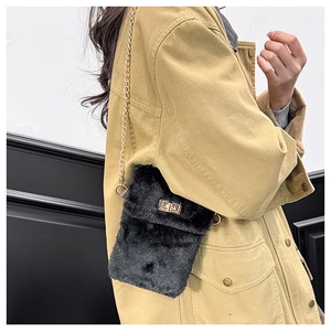 Detail of a black plush crossbody bag featuring a golden chain strap and a metal turn-lock