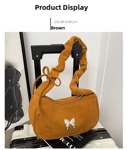 Détail du sac hobo en daim marron avec bandoulière plissée et papillon argenté