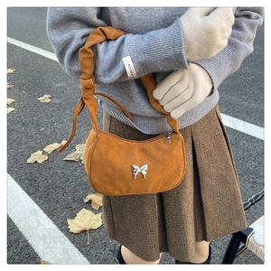 Detail of caramel suede baguette bag featuring silver butterfly buckle and ruched strap