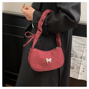 Close-up of wine red suede crescent bag featuring side bows and a silver butterfly charm
