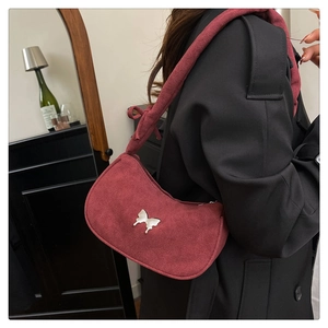 Detail of burgundy suede crescent bag with silver butterfly accent on a black wool coat