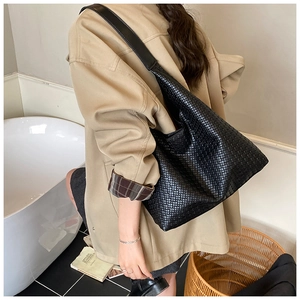 Detail of a large black woven leather tote bag showing a sleek braided pattern on shoulder