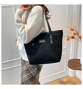 Detail of black suede tote bag featuring gold brand plate and rivet accents for commuting