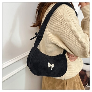 Detail of black suede underarm bag featuring a silver metal butterfly and bow strap