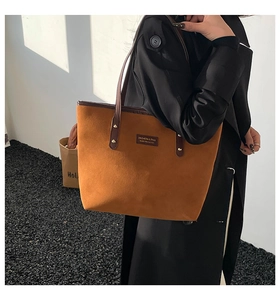 Close-up of brown suede tote bag with dark leather handles and fashion logo tag