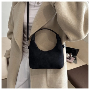 Détail du sac dumpling en daim noir avec boucles argentées porté par un mannequin