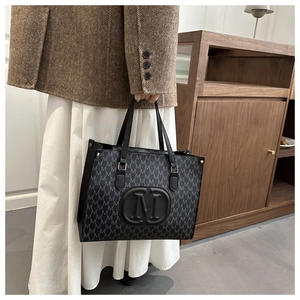 Detail of black leather tote bag with M-letter print and large embossed logo on model
