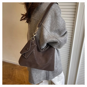 Detail of matte dark brown leather tote bag with small envelope pouch on a gray coat