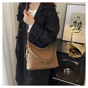 Close-up of brown litchi grain faux leather hobo bag on a model wearing a black coat