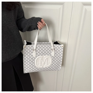 Detail of white tote bag with all-over M letter print and embossed large central logo
