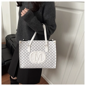 Detail of white tote bag featuring all-over M letter print and round logo emblem