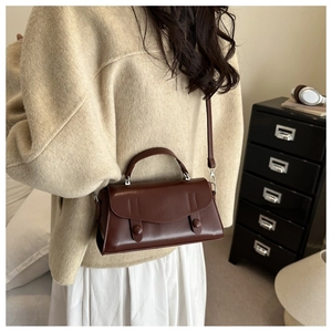 Macro shot of dark brown leather crossbody bag with vintage stitching on a retro cabinet