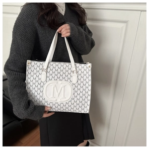 Close-up of the embossed M letter detail on white leather tote bag with pattern