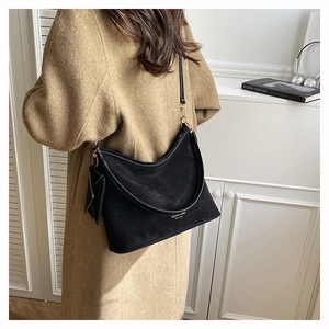 Close-up of black suede tote bag with white contrast stitching and mini charm pouch