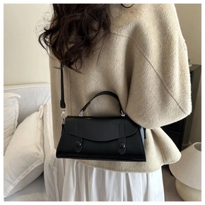 Close-up of a minimalist black PU leather crossbody bag worn by a model in a warm setting