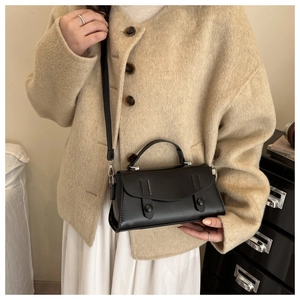 Detail of vintage black crossbody bag with round rivet straps and top handle on a model