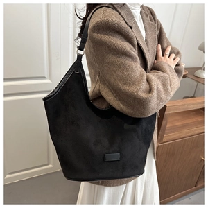 Close-up of black matte suede hobo bag with sleek shoulder strap on a herringbone blazer