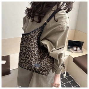 Detail of leopard print tote bag with black leather straps worn by model in a cozy setting