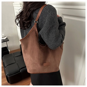 Detail of a dark brown suede tote bag with leather piping on a grey knit sweater