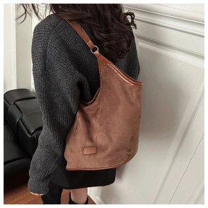 Detail of a brown suede hobo tote bag with a minimalist leather tag and slim shoulder strap