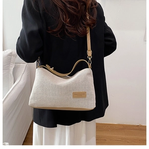 Borsa a tracolla in tela beige e pelle kaki indossata da una modella in un interno moderno