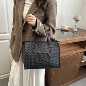 Chic black tote bag with M-letter print and handles shown in a lifestyle office setting