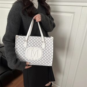 White tote bag with grey M-letter monogram print and top handles shown in indoor setting