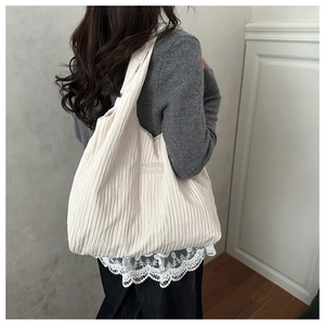 Detail of cream pleated canvas tote bag with FASHION label on model shoulder