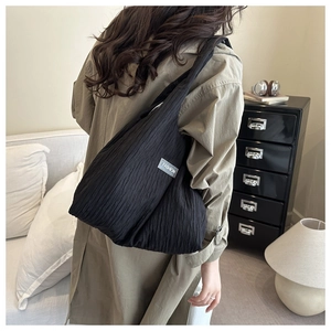 Detail of black pleated canvas tote bag showing wide strap and fashion woven label