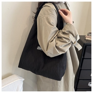 Detail of black pleated tote bag showing the side fashion label and textured fabric