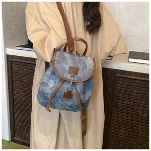 Blue denim backpack with brown leather trim shown on model in a casual setting