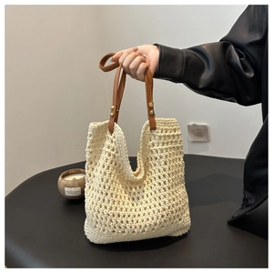 Detail of hand-woven straw tote with brown faux leather handles and gold rivet accents