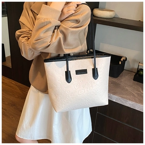 Detail of embossed large tote bag with cream texture, black handles, and fashion tag