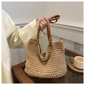 Close-up of hand-woven straw tote bag with brown leather handles and metal rivet details