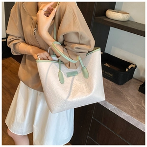 Close-up of white embossed tote bag with green handles and stylish cartoon patterns