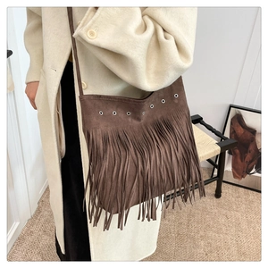 Détail d'un sac bohème en daim marron avec des œillets métalliques et de longues franges