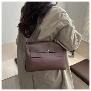 Sac bandoulière en cuir marron avec fermoir rotatif argenté porté par un mannequin en trench