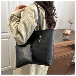 Detail of a large black leather tote bag with small zipper pouch shown on a shoulder