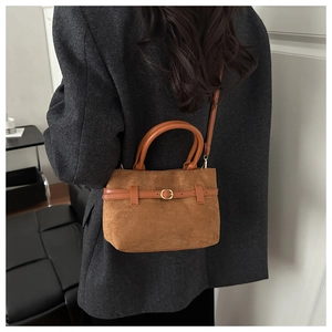 Détail du sac bandoulière en daim marron avec lanières en cuir et boucle en métal doré