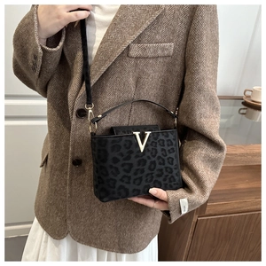 Sac bandoulière léopard avec fermoir V doré porté par un mannequin en blazer marron