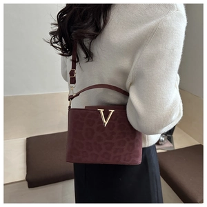 Détail du sac à main léopard bordeaux avec boucle en V dorée porté par un mannequin