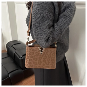 Détail du sac à bandoulière léopard avec boucle en V dorée sur une tenue décontractée